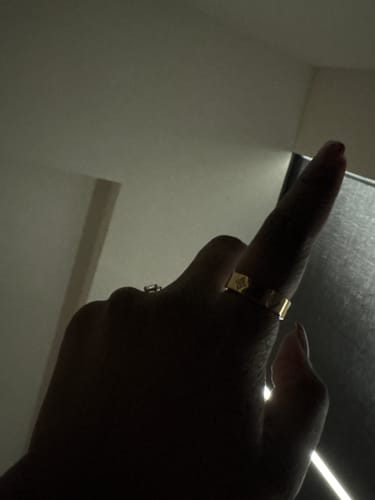 Close-up of a reviewer's hand wearing the gold Eloise Ring in dim lighting.