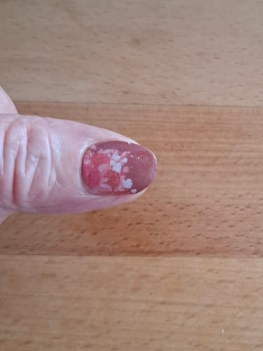 Nahaufnahme des Daumens eines Kunden mit der 'Dipped In Blooms' UV-Gel-Folie auf einem kurzen Nagel.