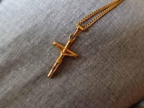 Primer plano del colgante Cross Minimal Oro de un cliente, sobre una superficie de tela gris.