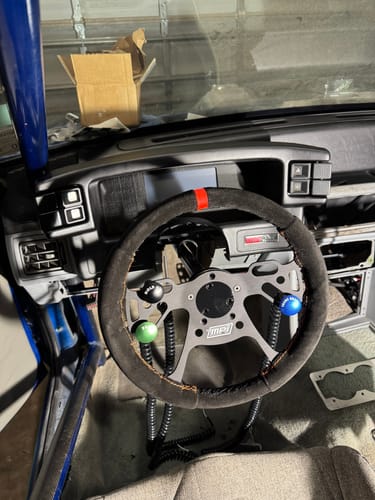 Customer's MPI Drag Racing Steering Wheel with black suede grip and an orange marker installed in a car.