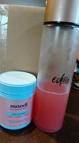 Customer's tub of moodi Pink Lemonade powder next to a bottle with the prepared pink probiotic drink.