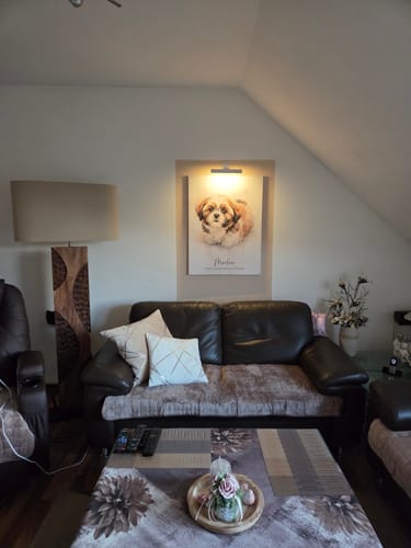 Rezensent zeigt die Holz Stehlampe AMAZONIA beleuchtet in der Ecke eines Wohnzimmers mit Dachschräge.