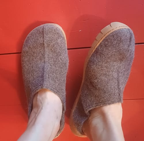 Asiakkaan harmaat Vaistoa Toive -paljasjalkatossut jalassa punaisella lattialla.