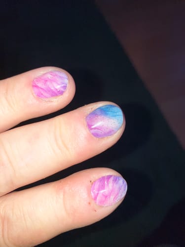 Hand einer Kundin mit UV-Gel-Nagelfolien in einem marmorierten, mehrfarbigen Design.