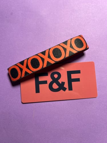 Customer's F&F Colorwheel Bracelet in black and orange with a repeating 'XOXO' pattern, resting on a branded card.