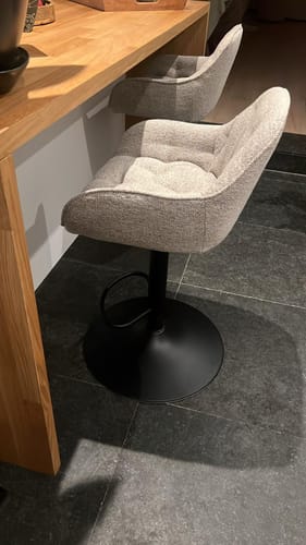 Recensent toont de beige Arvid verstelbare barkruk aan een houten bar.