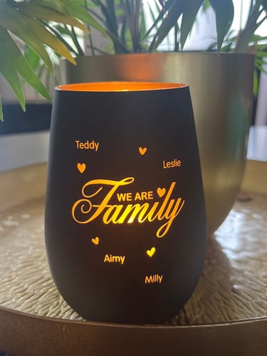Photo d'un client montrant le photophore noir mat allumé, avec la gravure 'We are Family' et des prénoms qui brillent.