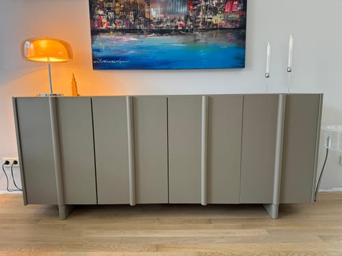 Recensent toont het modderkleurige WOOOD Basu dressoir in een woonkamer onder een schilderij.