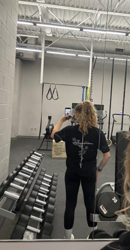 Reviewer in a gym showing the back of the 'Floral Cross' Women’s Oversized T-Shirt.