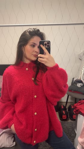 Kundin in einem leuchtend roten Oversized-Cardigan "CozyGlam" mit goldenen Knöpfen.