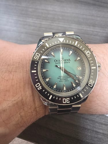 A customer's wrist wearing the Oceaneva watch, highlighting its mint burst dial and a swapped metal bracelet.