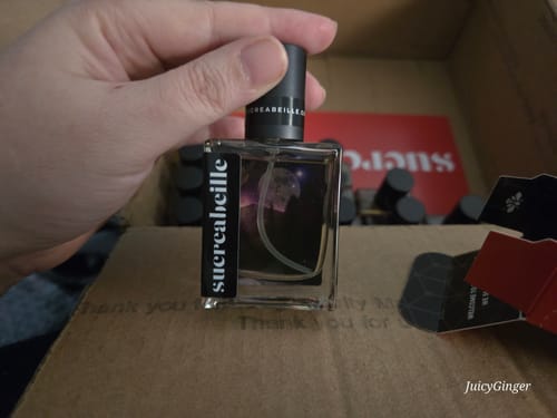 Reviewer holding a square glass bottle of Solstice perfume inside an open shipping box.