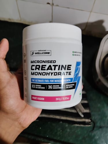 Reviewer holding a white tub of Wellcore Micronised Creatine Monohydrate in the Fruit Fusion flavor.