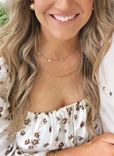Customer wearing a delicate gold necklace with G, heart, and M initial charms.