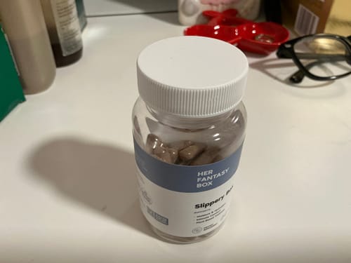 Customer's clear bottle of Slippery Box capsules with a white lid, shown on a white counter top.