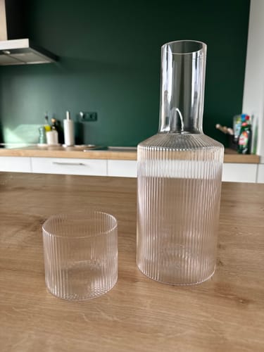 Recensent toont de heldere, geribbelde Ferm Living Ripple Karaf met een bijpassend glas op een keukenaanrecht.