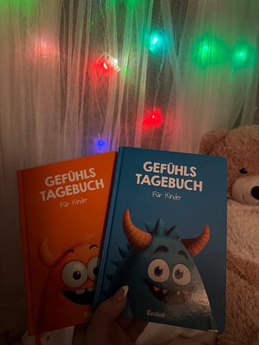Rezensent hält zwei Gefühlstagebücher für Kinder, ein orangefarbenes und ein blaues, in der Hand.
