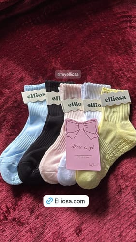 Reviewer's colorful collection of Elliosa Grip Basics socks, including the soft pink pair, on a red surface.
