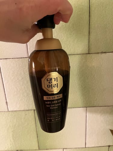 Клиент натиска помпата на шампоана Doori New Gold Special на фон от плочки.