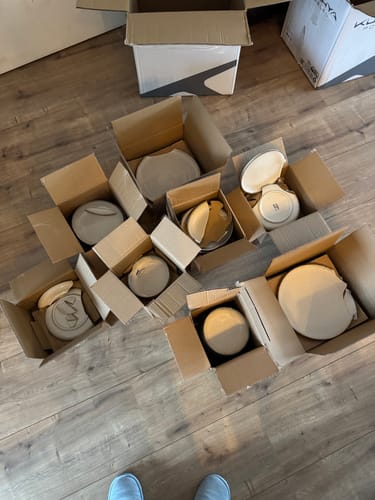 Recensent toont de kapotte, beige Loods serviesset die gebroken is aangekomen in meerdere dozen.