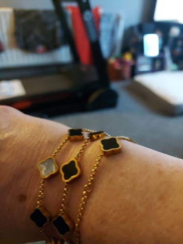 Close-up of a reviewer's wrist wearing multiple Celine Clover Bracelets with black and white motifs.