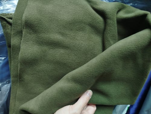 Customer holding a large piece of olive green Plain Anti Pill Polar Fleece Fabric, showing its texture and drape.