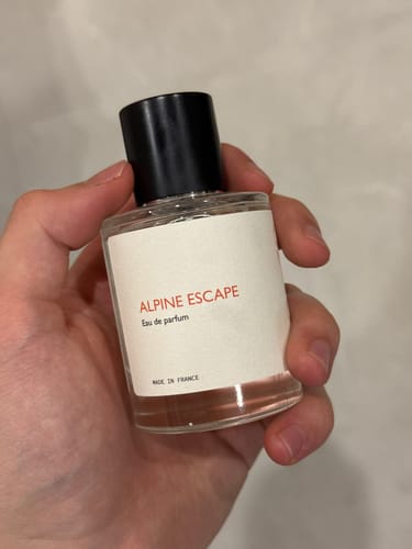 A customer's hand holding the clear glass bottle of Alpine Escape perfume.