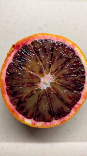 Kunde zeigt eine aufgeschnittene, sehr dunkelrote Blutorange aus der Bio Orangen-Mixbox.