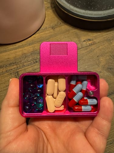 Customer holding an open pink Mission Case in their palm, showing three compartments filled with various pills.