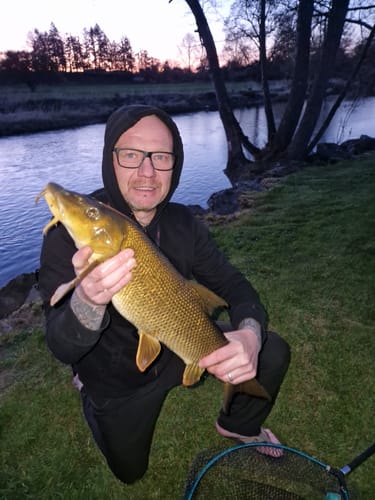 Klant geknield aan een rivier die een grote barbeel vasthoudt.