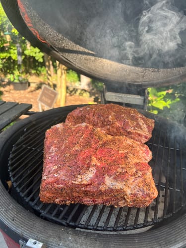 Customer's seasoned USDA Choice Bone-In Short Ribs on a round smoker with smoke rising.