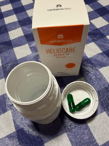 レビュアーのヘリオケア ウルトラD。箱と開けたボトル、蓋の上にある2つの緑のカプセル。