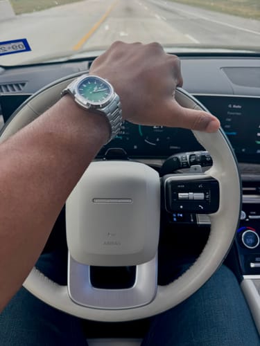 Customer wearing the silver Lucky Fours® Caspian watch with a green dial while holding a steering wheel.