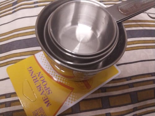 Customer's set of nested, stainless steel AZ Measuring Cups shown on their yellow packaging.