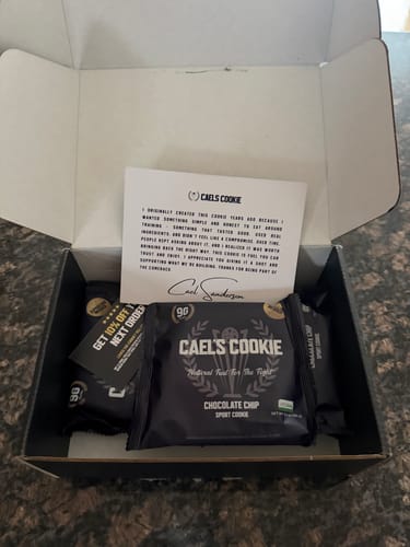 Reviewer's open box containing several Cael's Chocolate Chip Cookies in dark packaging.