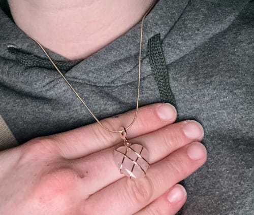 Customer wearing a necklace with a heart-shaped rose quartz pendant wrapped in gold wire.