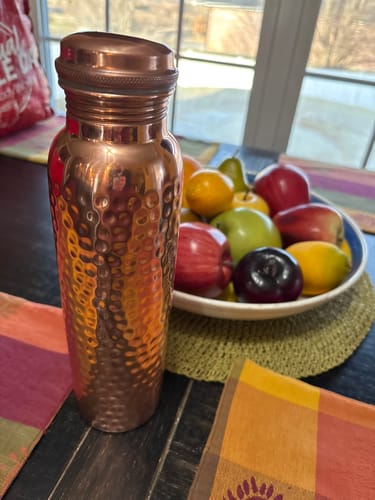 Customer's hand-hammered copper water bottle sitting on a table next to a bowl of fruit.