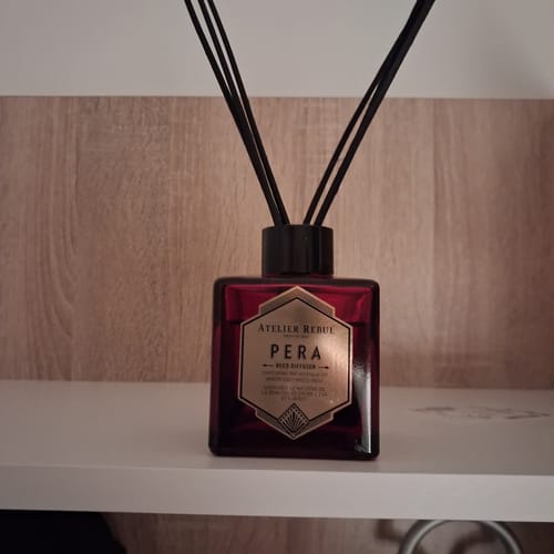 Recensent toont de rode Pera Geurstokjes met zwarte stokjes op een plank.