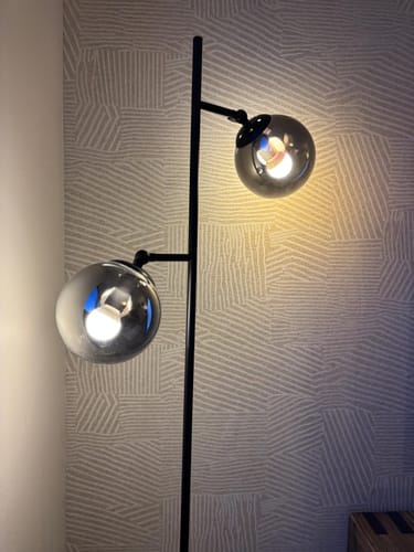 Recensent toont de QAZQA Pallon vloerlamp met de twee bollen van rookglas aan.