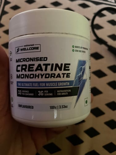 A customer holds their white tub of Wellcore Micronised Creatine Monohydrate against a patterned background.