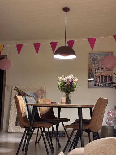 Beoordelaar toont de rode by fonQ Bloop hanglamp, brandend boven een eettafel in een feestelijke setting.