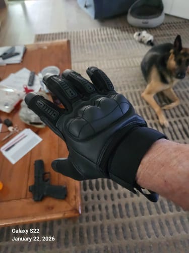 Customer's hand wearing a black Onslaught Glove, with a handgun visible on a table in the background.