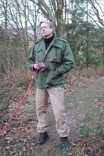 Reviewer standing outdoors in a wooded area wearing the green Aggressor M-1951 Field Jacket.