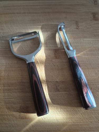 Rezensent zeigt das Asiatische Premium Schäler Set mit beiden Schälern auf einem hölzernen Schneidebrett.