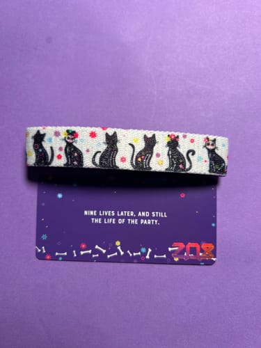 Customer's white Dia De Los Meowtos Bracelet with a colorful cat pattern, displayed on its purple backing card.