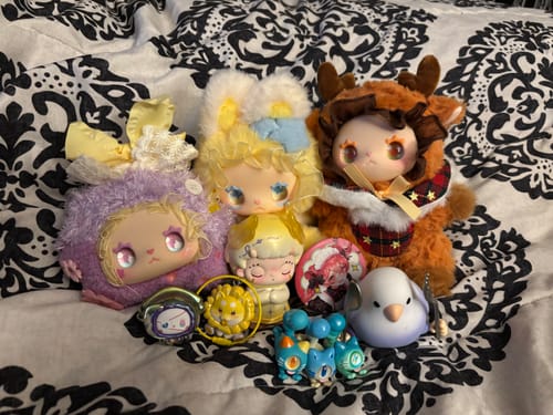 Reviewer's collection of colorful Lovely EMMA Floral Seasons plush toys and other figures on a patterned bedspread.