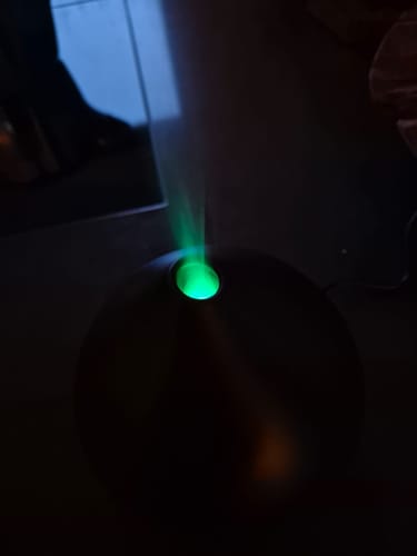 Klant toont de zwarte Unity 2.0 Aroma Diffuser in het donker, die nevel met een helder groen licht uitstoot.