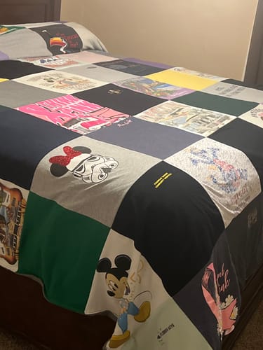 Customer's colorful Premium T Shirt Quilt, made from many different shirts, spread out on a bed.
