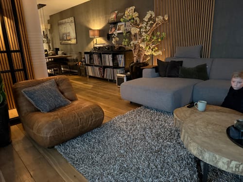 Recensent toont de Wyatt Fauteuil van cognac-leer in een sfeervolle woonkamer.