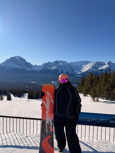 Reviewer wearing the black retro track snow jacket with reflective piping while holding a snowboard on a mountain.